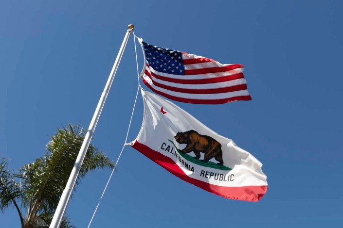 The American and California flags waving against a clear blue sky.