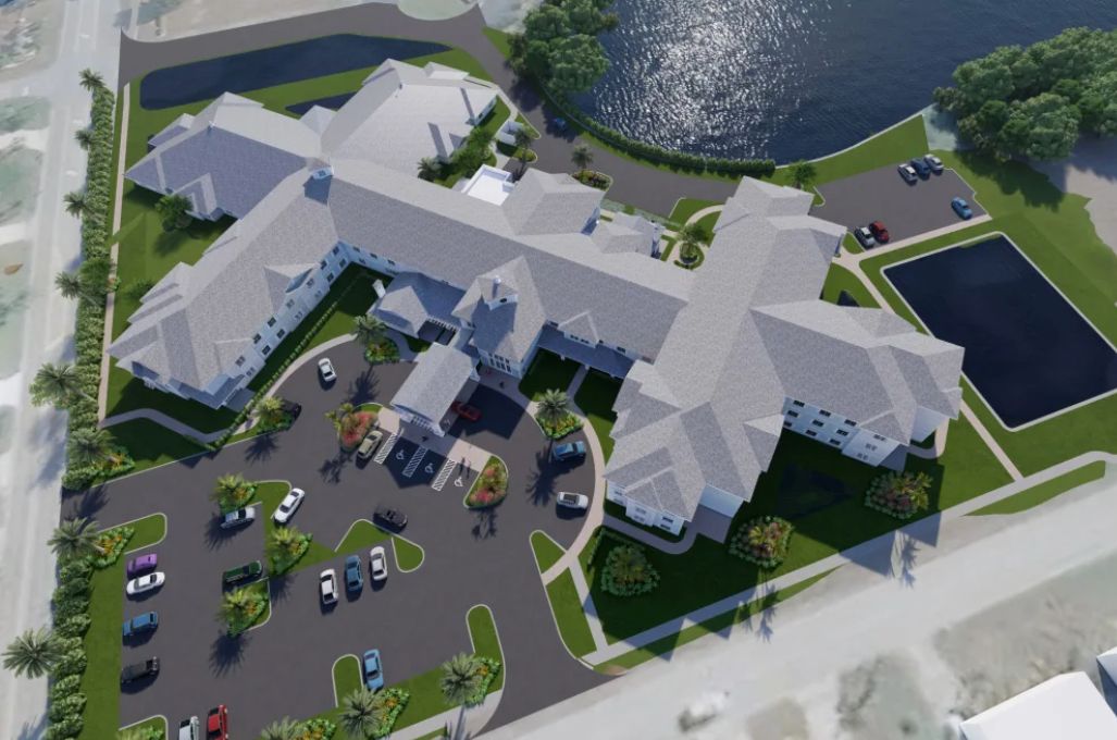 An aerial view of a large, cross-shaped building complex with a parking lot and nearby pond.