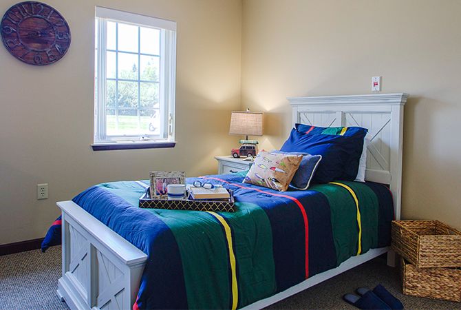 A cozy bedroom with a colorful bedspread, illuminated by a bedside lamp and natural light from the window.