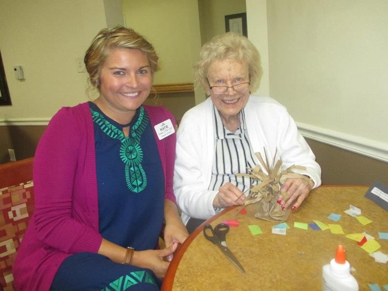 Two women sitting at a table, working on a crafting project.