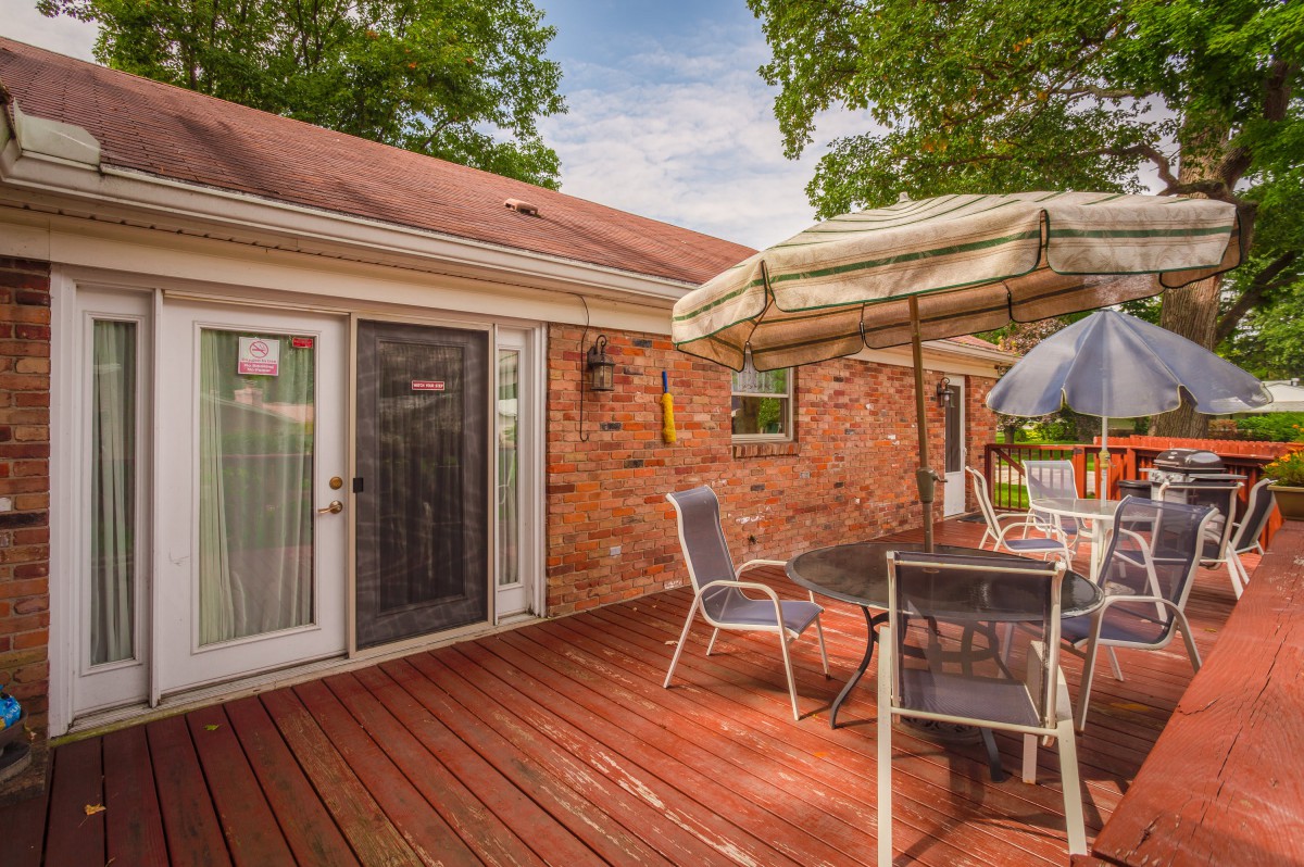 A cozy outdoor deck with a dining set under an umbrella, adjacent to a brick house.