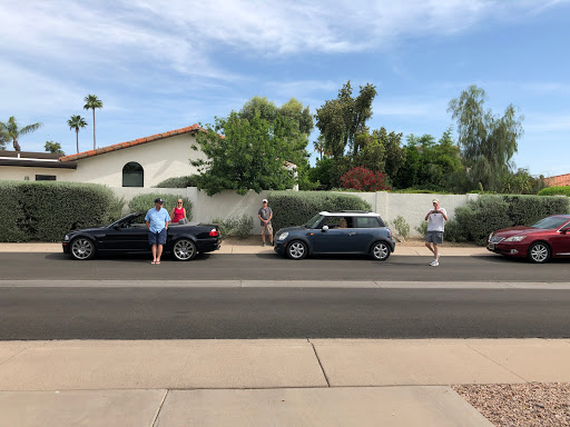 A group of people interacting near parked cars on a sunny day.
