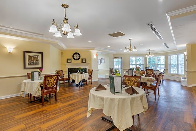An elegantly decorated dining room with several tables and chairs, featuring a chandelier and large windows.