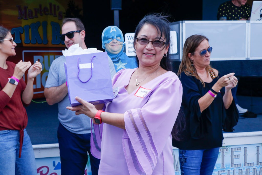 A woman holding a gift bag while smiling at an outdoor event.