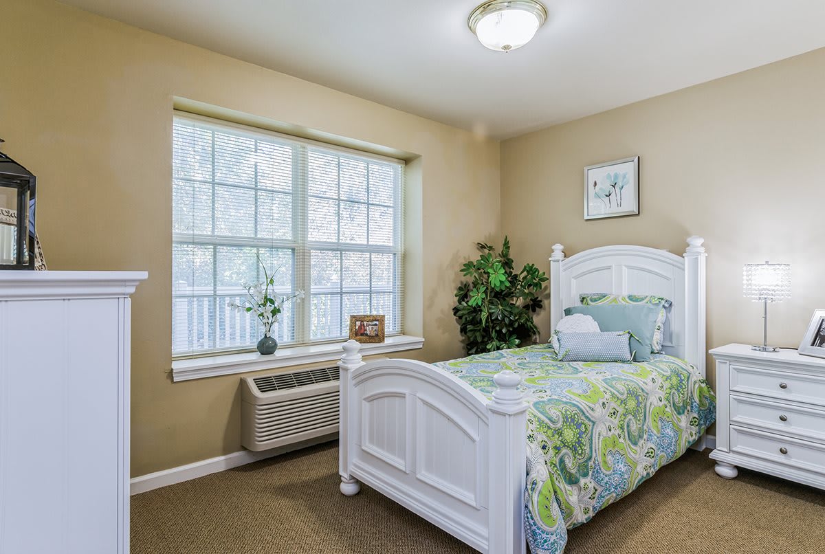 A cozy bedroom with a single bed, green bedding, and a large window letting in natural light.