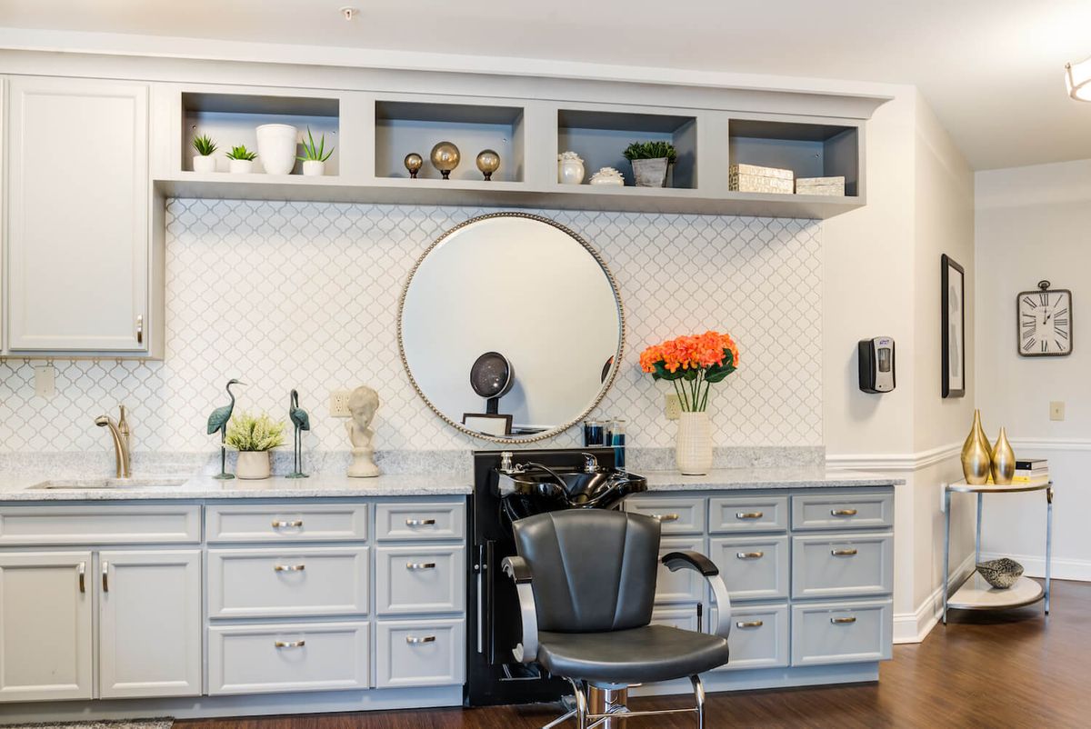 A modern salon interior featuring a hairdressing chair, a large round mirror, and decorative elements such as shelves and flowers.
