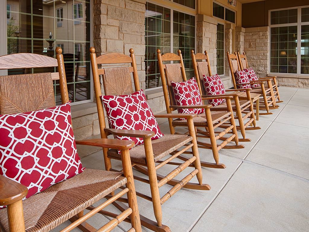 Wooden rocking chairs with red patterned pillows lined up on a porch.