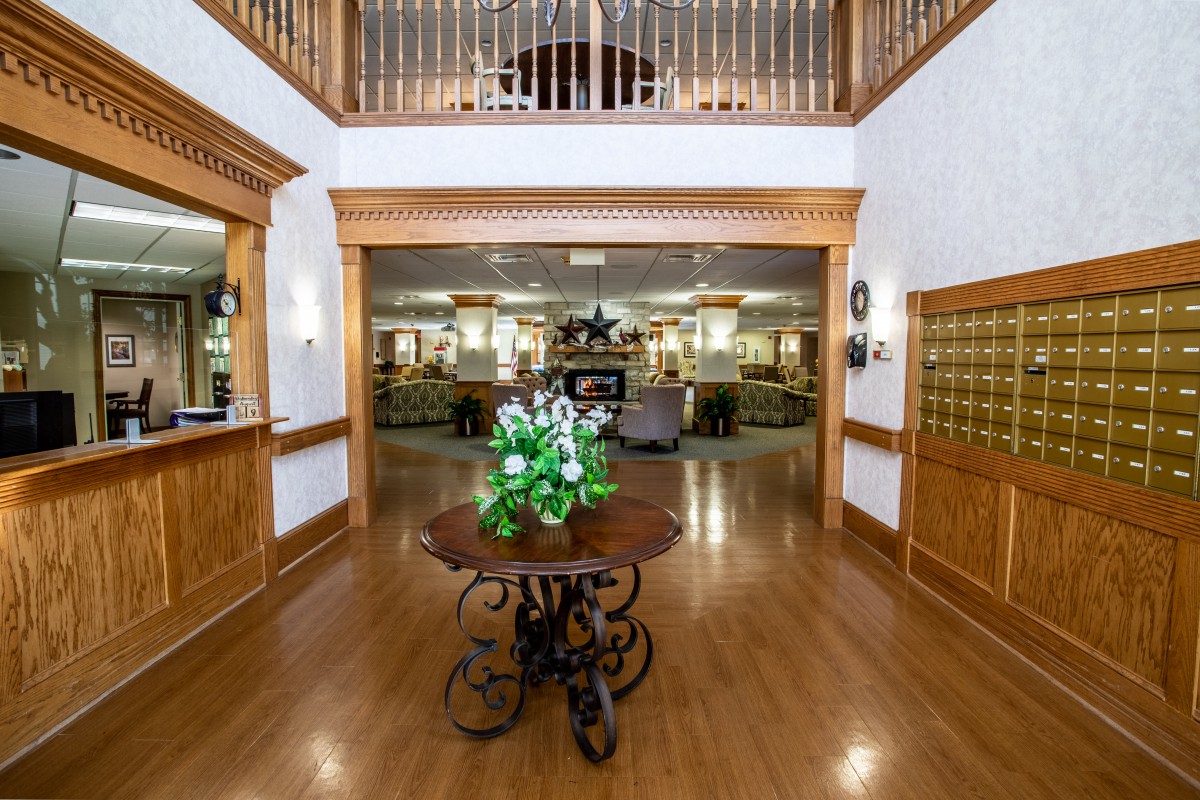 A spacious lobby with wooden flooring, featuring a central table adorned with flowers and an overlooking balcony.