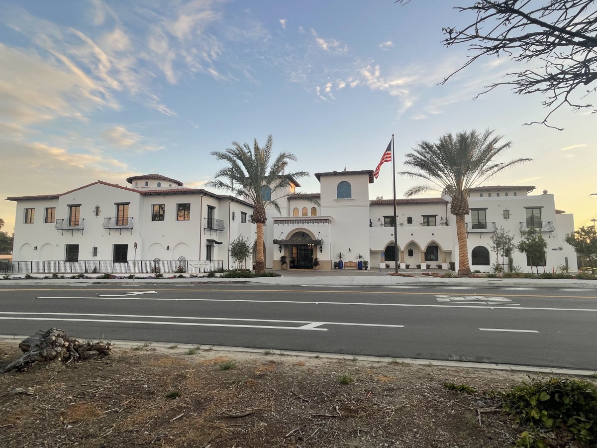 A scenic view of a large building with palm trees and a flag, captured at sunset from across the road.