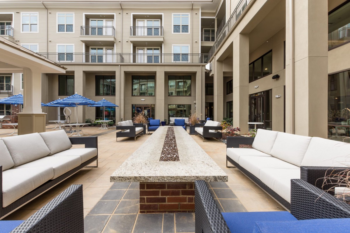 Modern outdoor seating area with couches and a central fire pit in an apartment courtyard.