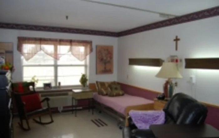 A hospital room with a bed, chair, and table by the window.
