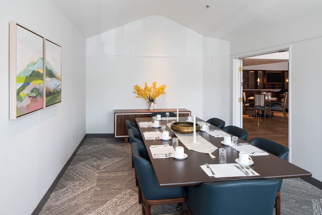 A modern dining room with a large table set for a meal, featuring elegant decor and a vase of yellow flowers.