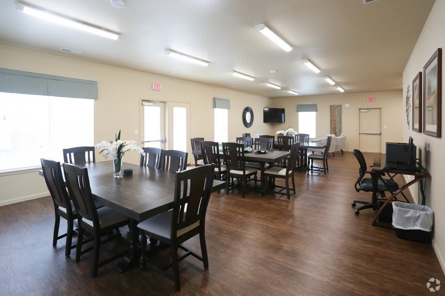 A spacious dining room with multiple tables and chairs, featuring wooden flooring and ample lighting.
