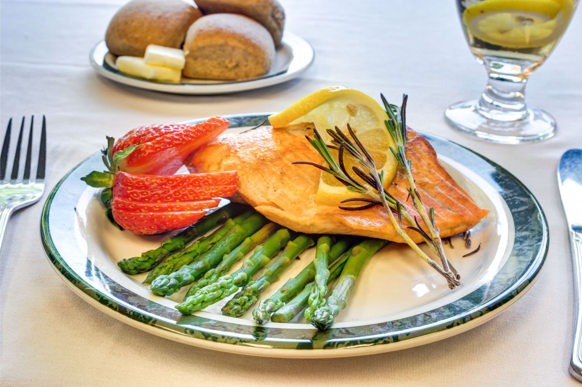 A gourmet meal featuring grilled salmon served with fresh asparagus, strawberries, and garnished with lemon and rosemary.