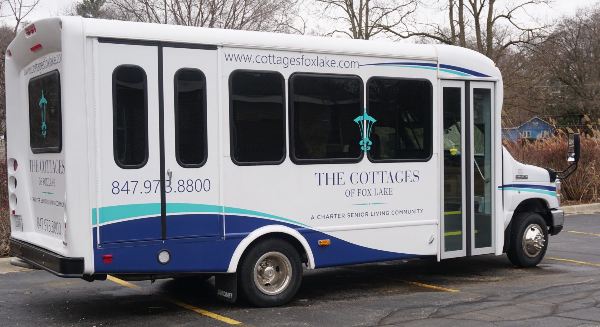 A shuttle bus featuring an advertisement for 'The Cottages by the Lake' is parked in a lot.