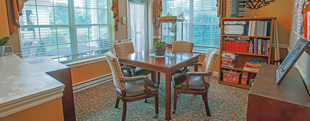 A cozy dining area with a wooden table and four cushioned chairs, surrounded by large windows and adorned with a small potted plant.