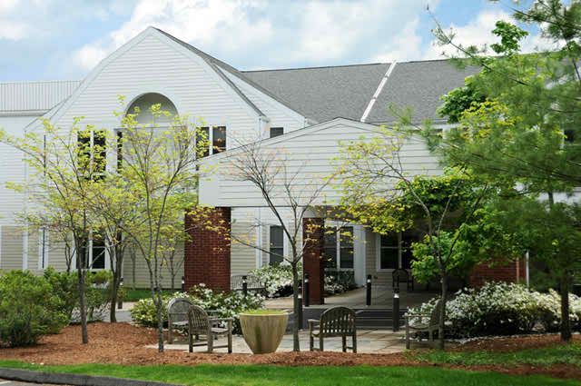 A white building surrounded by trees and benches in a landscaped area.