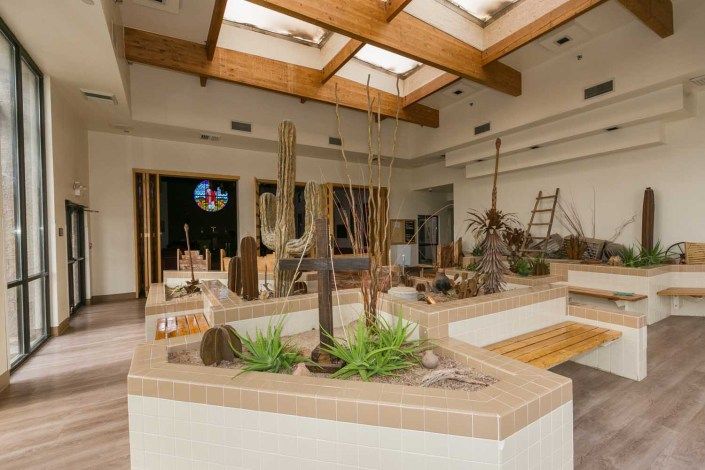 A spacious art gallery featuring sculptures and an indoor garden with natural light streaming through skylights.