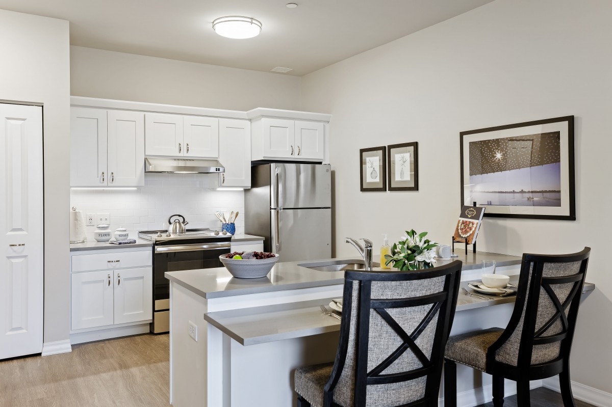 A modern kitchen with white cabinets and a dining area, featuring stainless steel appliances and elegant decor.