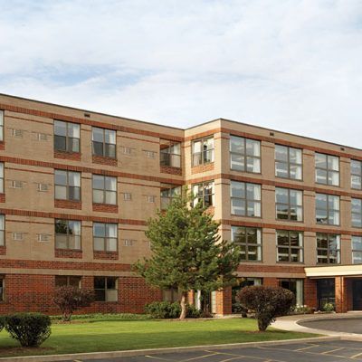 A brick residential apartment building with a well-maintained landscape and trees in front.