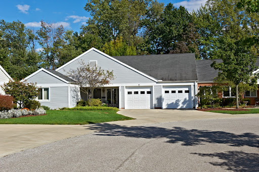 A modern single-story house with a gray exterior and two garage doors, surrounded by lush greenery.