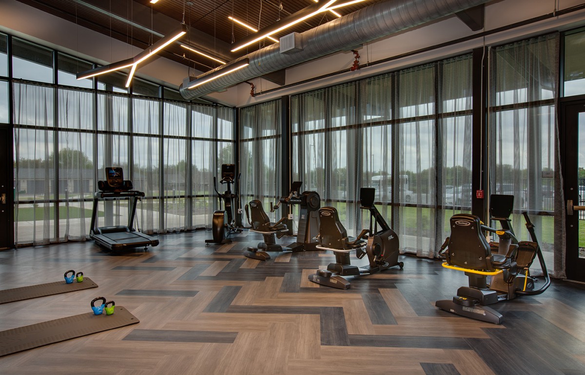 A modern gym with large windows, featuring treadmills and stationary bikes.