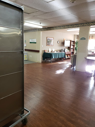 A spacious common area with wooden flooring and ample natural light, featuring seating and decor.