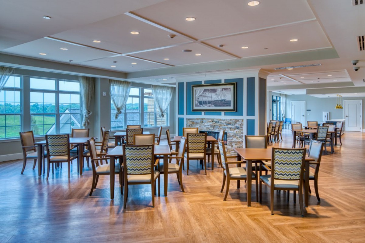 A spacious dining area with neatly arranged tables and chairs, featuring wood flooring and ample natural light.