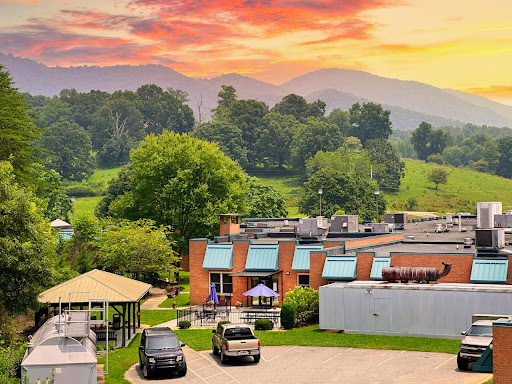 A picturesque sunset over rolling mountains, with a charming building and lush greenery in the foreground.