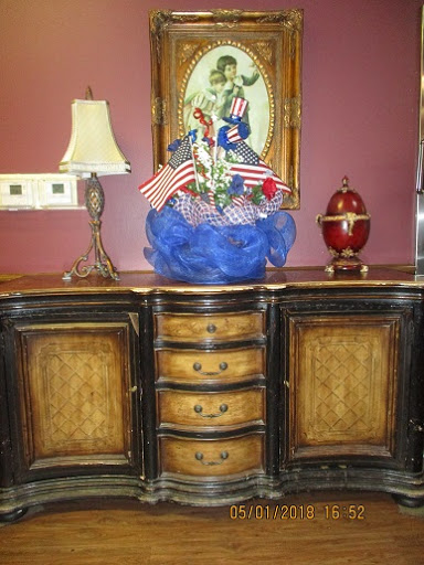 A beautifully crafted wooden cabinet with decorative elements, including a lamp and a floral arrangement featuring small flags.