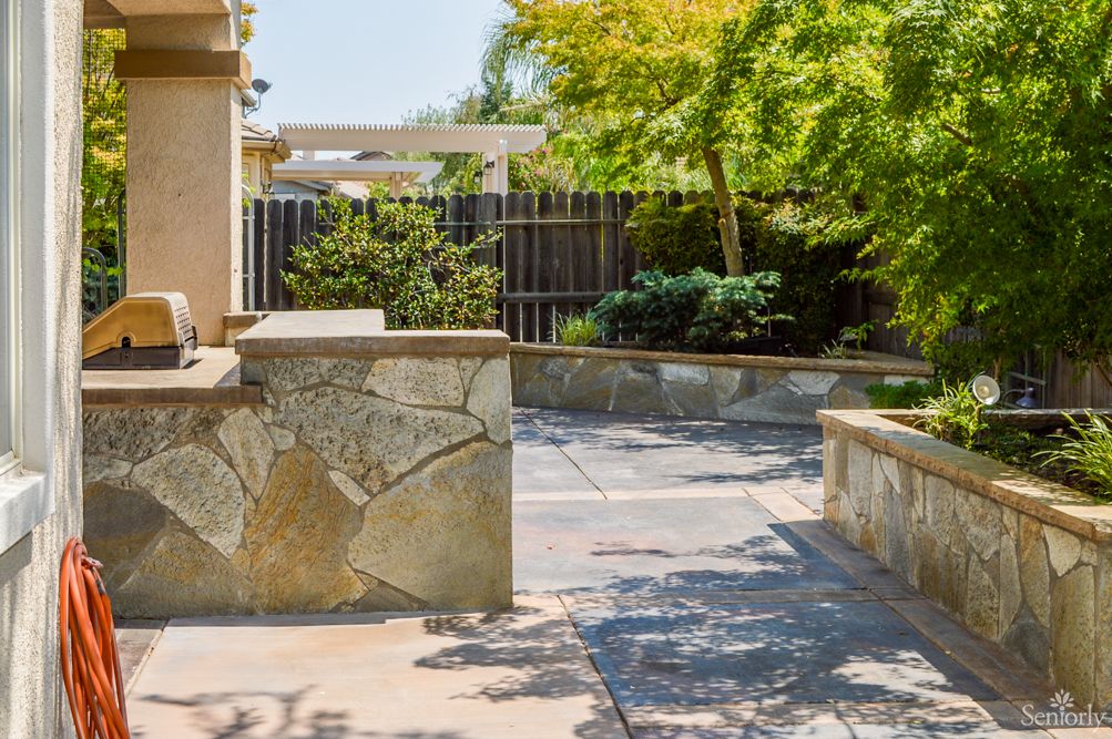 A sunny patio area with stone walls and lush greenery in the background.