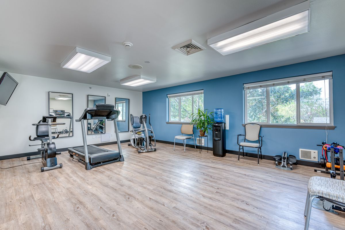 A well-lit exercise room with a treadmill and fitness equipment.