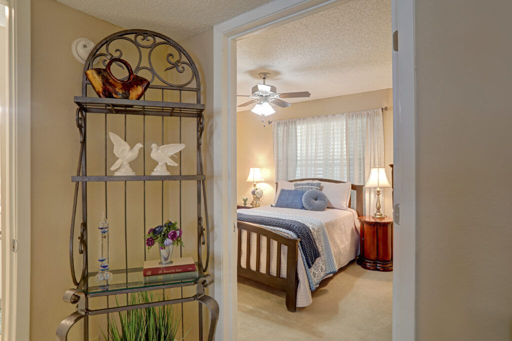 A cozy bedroom with a comfortable bed, wooden side tables, and warm lighting, viewed through an open door.