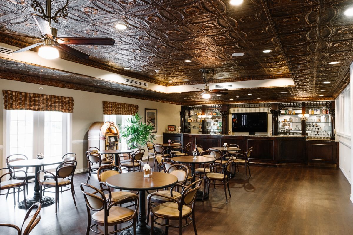 A cozy restaurant interior with a decorative ceiling, featuring tables and chairs arranged near a bar area.