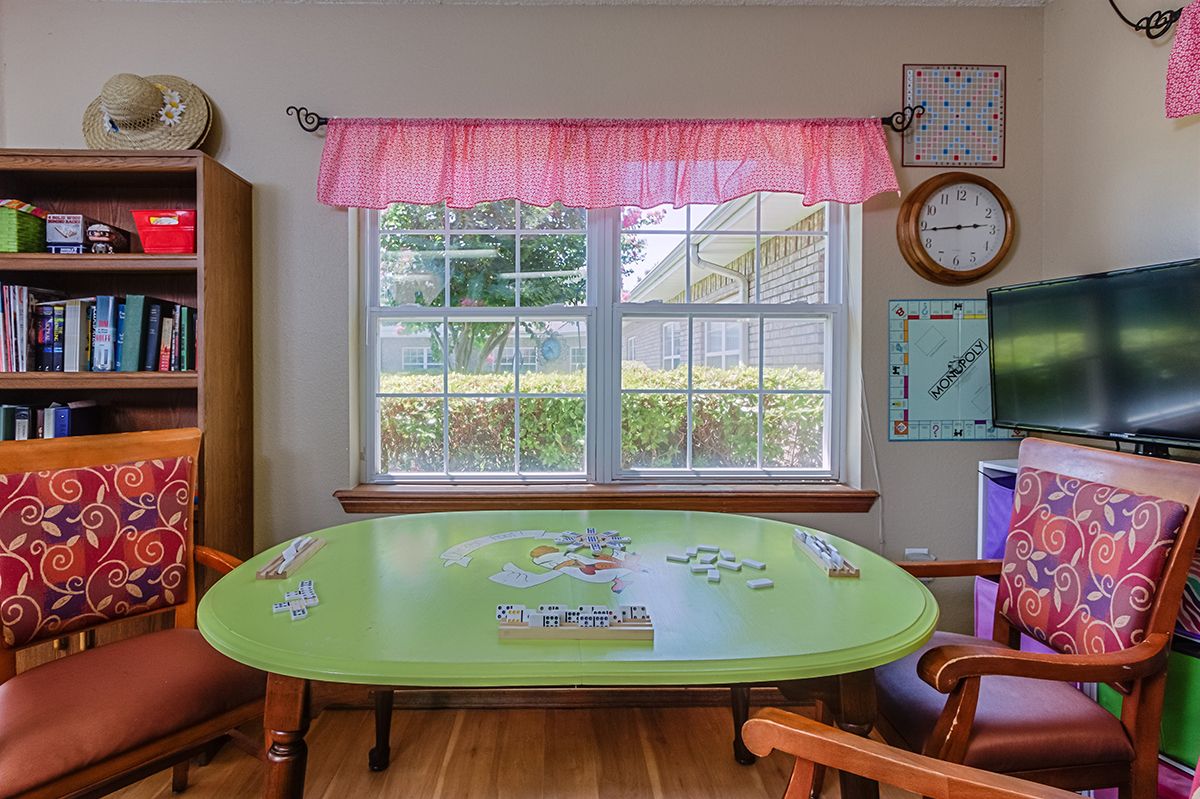 A cozy room with a green table featuring a puzzle in progress, surrounded by wooden chairs and adorned with pink curtains.