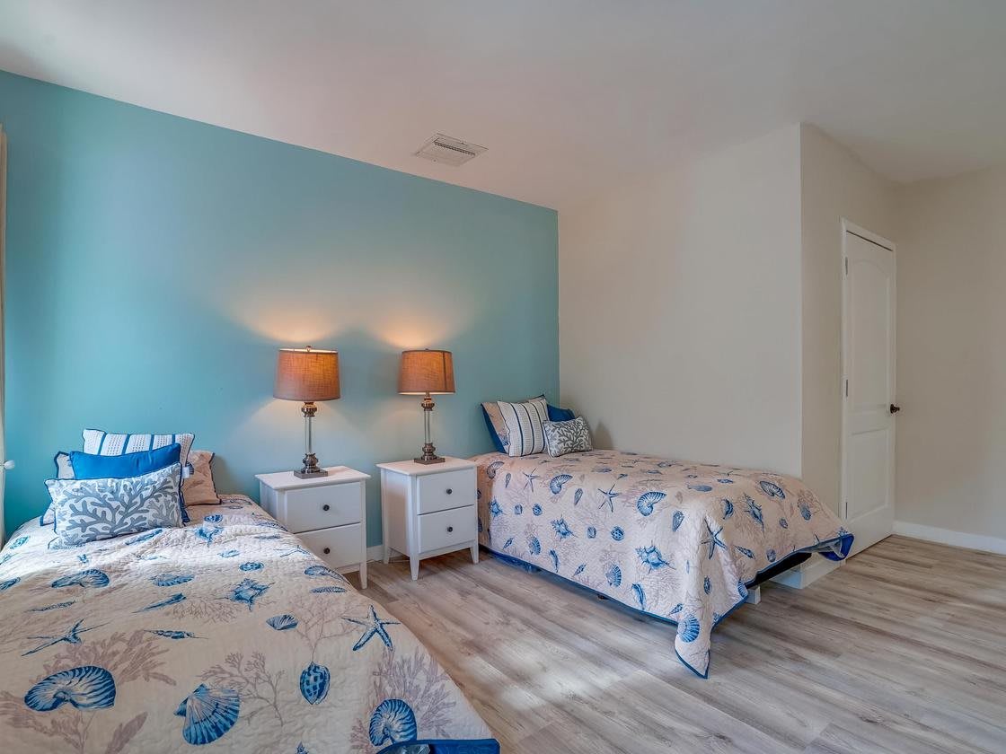 A cozy bedroom with twin beds featuring floral bedding, complemented by a blue accent wall and matching lamps on nightstands.