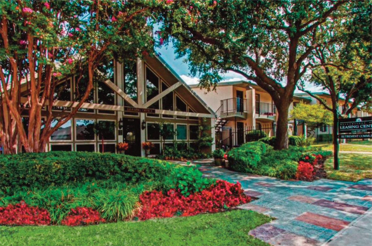A beautiful house with a lush garden and pathway, surrounded by trees and vibrant flowers.