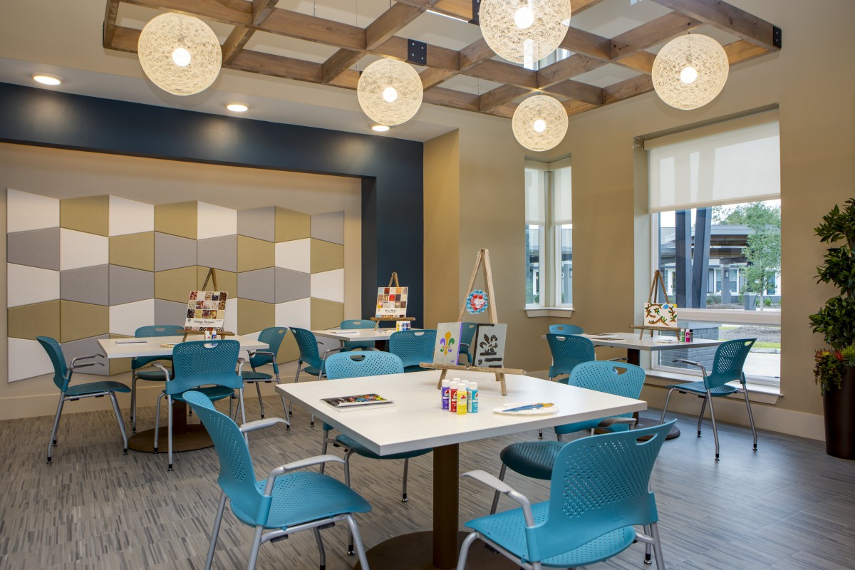 A modern art room featuring blue chairs, white tables, and creative lighting.