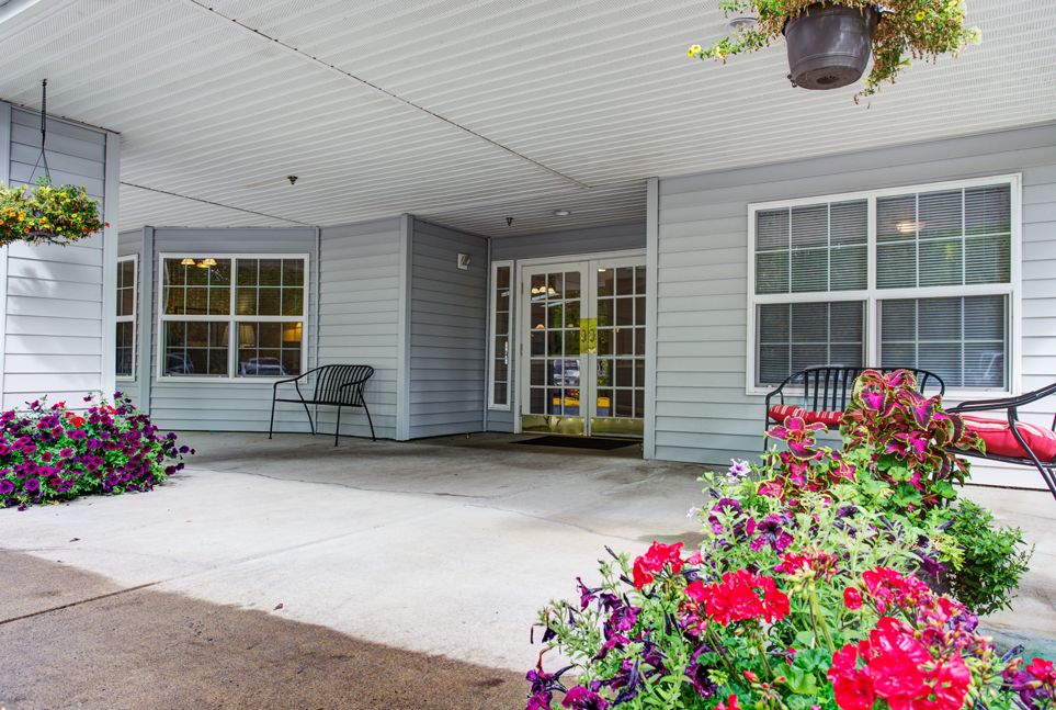 A welcoming building entrance with a porch adorned with vibrant flowers and a bench.