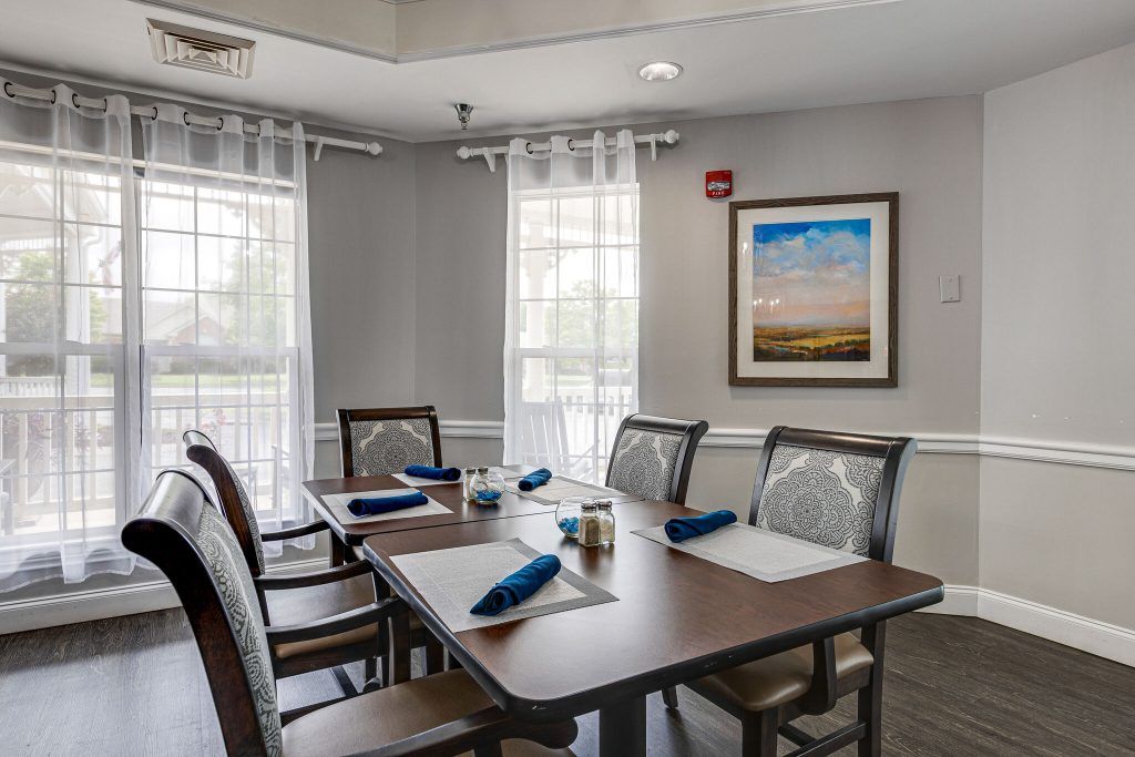 A neatly arranged dining room with a table set for four, featuring blue napkins and placemats, with sunlight streaming through the windows.