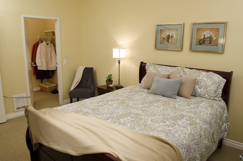 A cozy bedroom with a neatly made bed, decorative pillows, and soft lighting from a floor lamp beside the bed.