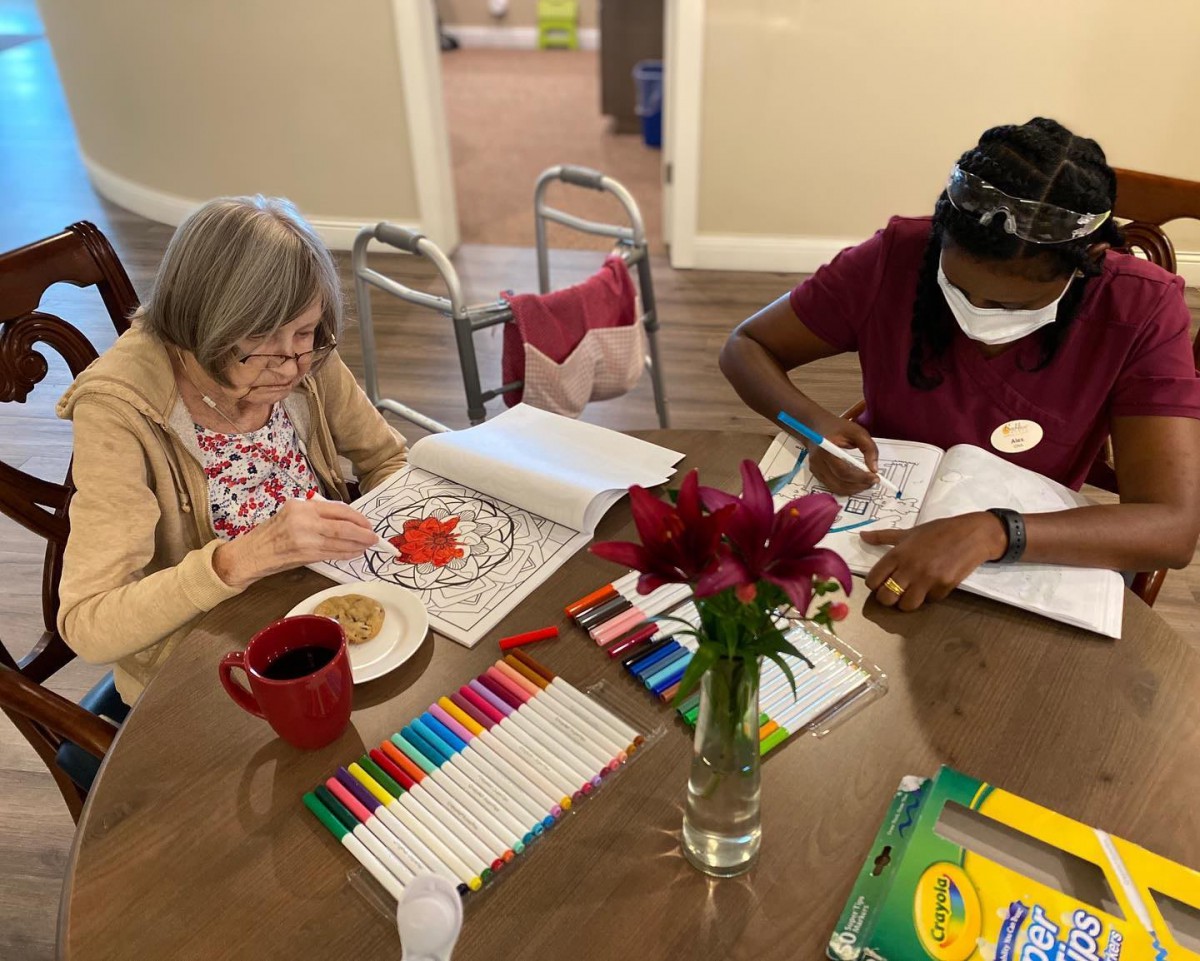 Two individuals engaged in a coloring activity at a table, surrounded by markers and flowers.