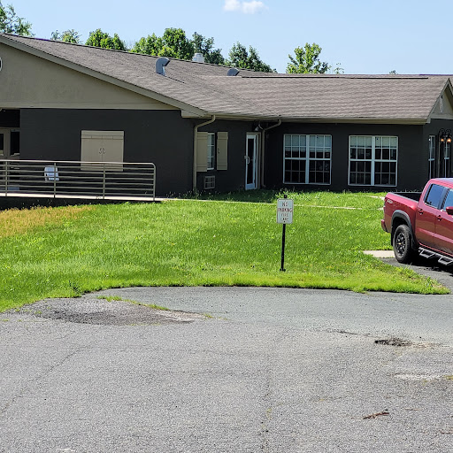 A red truck parked in front of a building surrounded by green grass on a sunny day.
