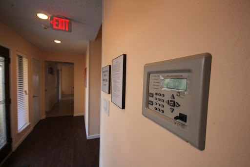 A hallway featuring a security control panel and an emergency exit sign.