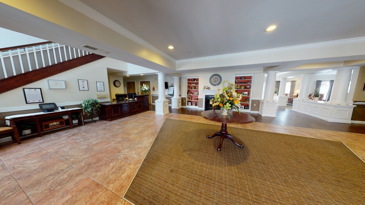A spacious and welcoming lobby area with a reception desk, bookshelves, and a central table adorned with a floral arrangement.