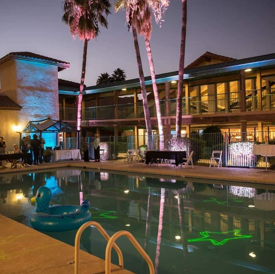 A nighttime scene at a hotel with a lit-up swimming pool and palm trees.
