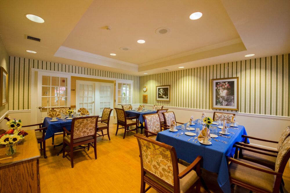 A cozy dining room with blue tablecloths and elegant place settings, featuring decorative wall art and comfortable seating.