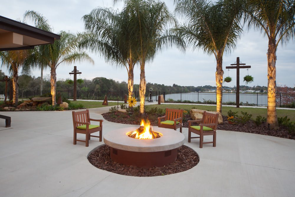 An inviting outdoor area with a fire pit surrounded by chairs, overlooking a scenic lake and framed by palm trees.