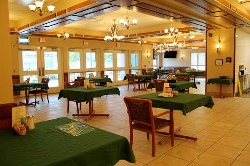 A spacious dining area featuring tables with green tablecloths and ample natural light from the windows.