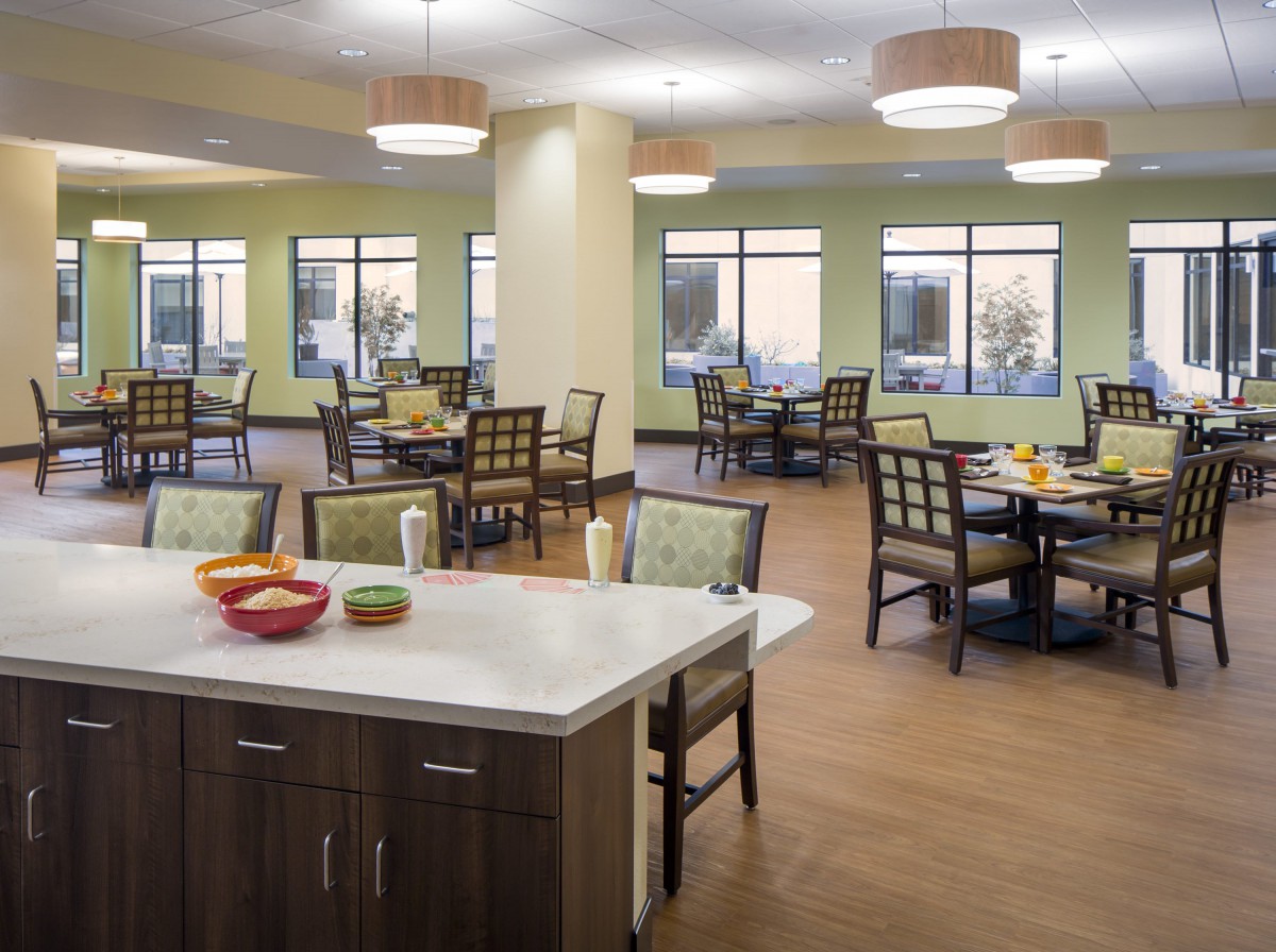 A modern dining area with multiple tables and chairs, featuring ample lighting and large windows.